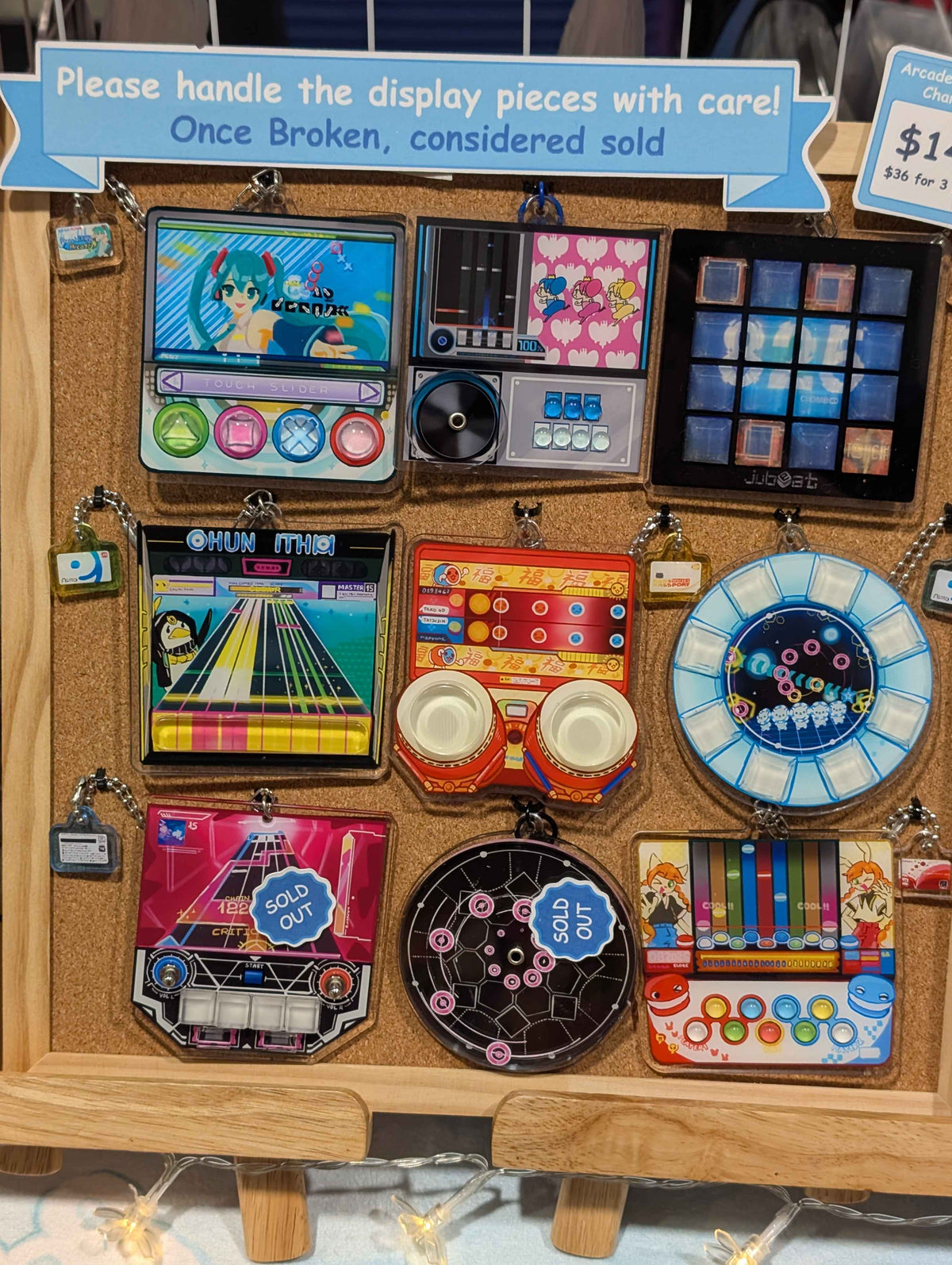 A collection of colorful mini keychains and charms featuring retro music instruments, game screens, and cartoon designs, arranged on a white fabric background.